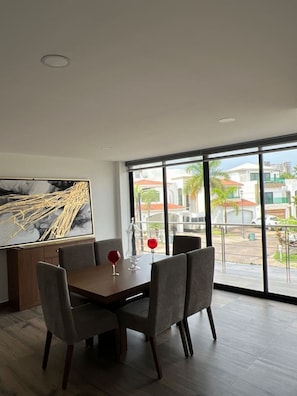 Ein Essbereich mit Tisch und Stühlen, ein großes Fenster mit Blick auf Gebäude und ein Gemälde an der Wand.