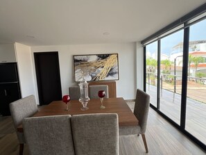 A dining area with a wooden table, grey upholstered chairs, and a large window offering a view of buildings and greenery. - departamento en isla marina mazatlan (Mazatlan)
