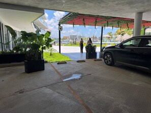 A covered outdoor area with a car parked to the right, potted plants, and a view of the marina in the background. - departamento en isla marina mazatlan (Mazatlan)