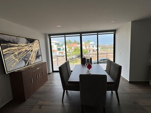 Ein Essbereich mit großem Fenster, einem Esstisch, Stühlen, einem Schrank und einem Flachbildfernseher.