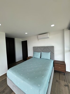 Ein Schlafzimmer mit einem Bett, Nachttischen, einer Wand-Klimaanlage und einer Tür.