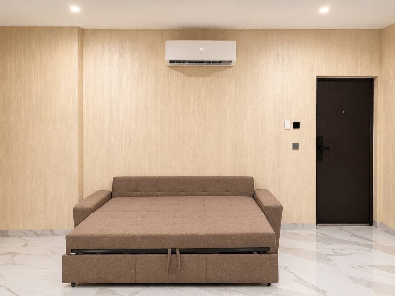A room with a bed, an air conditioning unit, a door, and a light switch.