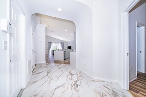 A hallway with a marble floor leading to a kitchen area. - 4-Bedroom Pool Home Near Disney | 2 Master Suites | Sleeps 10 (Clermont)