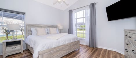 A bedroom with a bed, a nightstand, a TV, and a window with curtains.