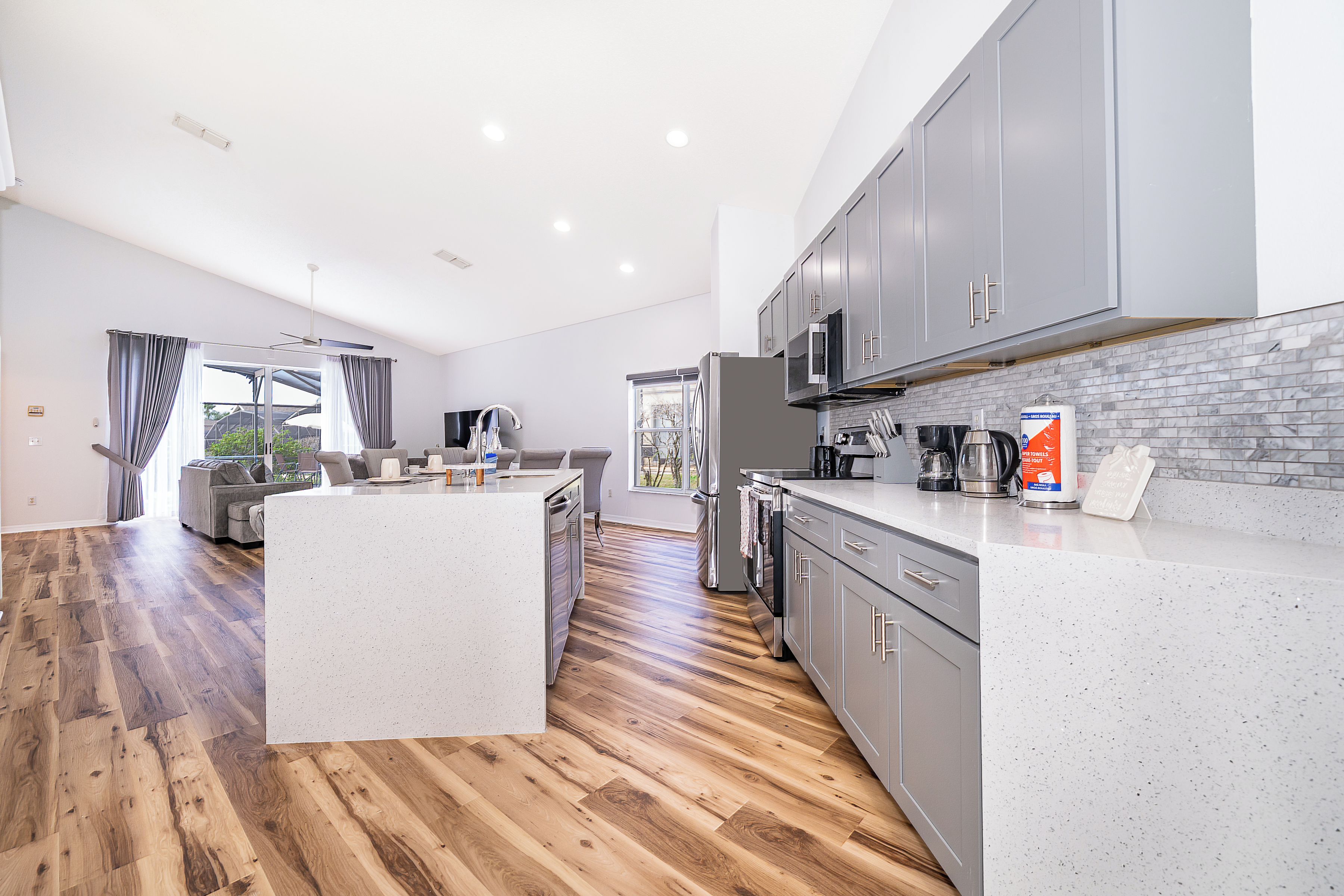 A modern kitchen with grey cabinets, a large island, and a dining area with a grey sofa.