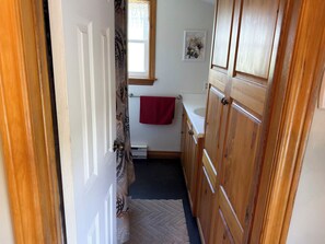 A narrow hallway leading to a bathroom with wooden cabinets, a white sink, and a red towel hanging on a rack.