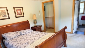 Une chambre à coucher avec un lit en bois, une table de chevet, une lampe et une porte donnant sur une autre pièce.