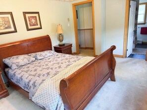 Un dormitorio con cama de madera, una mesita de noche, una lámpara y una puerta que da a otra habitación.
