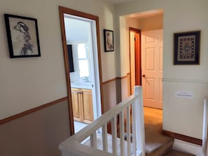 Un couloir avec un escalier, des œuvres d’art encadrées accrochées aux murs et un panneau d’avertissement indiquant que les marches sont étroites.
