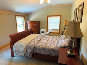 Une chambre à coucher comprenant un lit, une commode, un climatiseur, une lampe et des tableaux encadrés accrochés au mur.