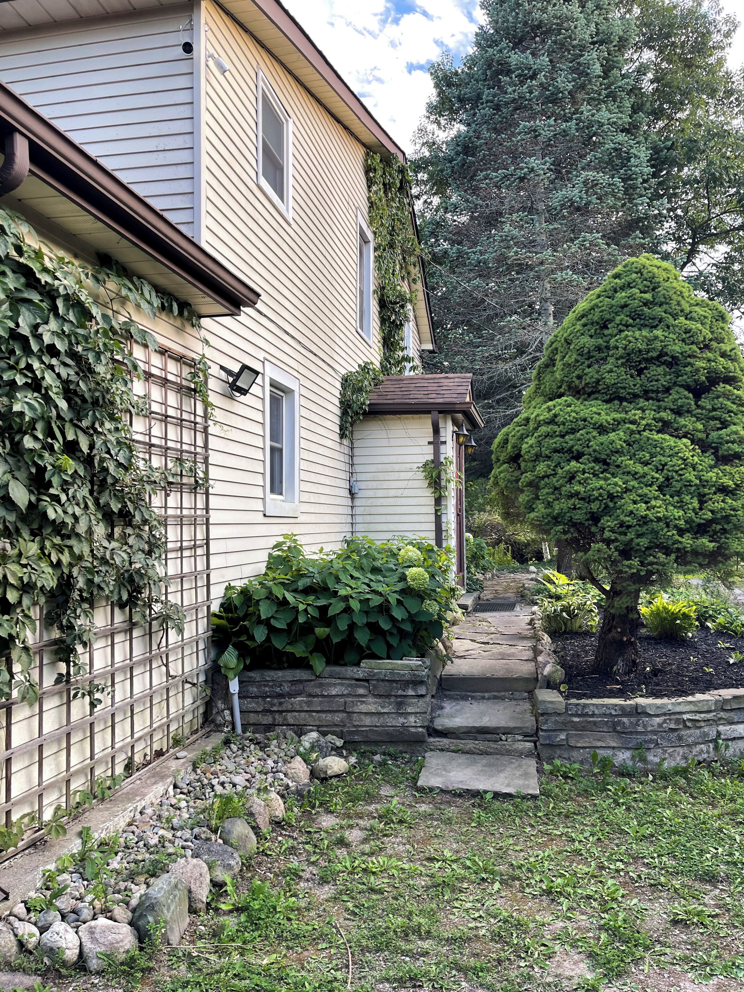 Une maison avec un chemin de pierre menant à la porte d’entrée, entourée de verdure et d’un petit arbre.