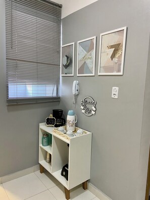 A room with a white console table, a coffee maker, a kettle, and a shelf with a jar. There are three framed artworks on the wall and a wall-mounted phone. - 103 Apto Lindo e Delicado  (Belém)