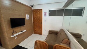 Ein Zimmer mit einem an einer Holzwand montierten Flachbildfernseher, einer Couch, einem Korbsessel und einer Tür mit einem Rauchverbot-Schild.