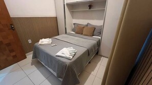 A hotel room with a bed, a bedside table, a wall-mounted shelf, and a door. - 103 Apto Lindo e Delicado  (Belém)