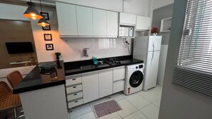 Uma cozinha moderna com armários brancos, bancada preta, máquina de lavar e micro-ondas embutido.