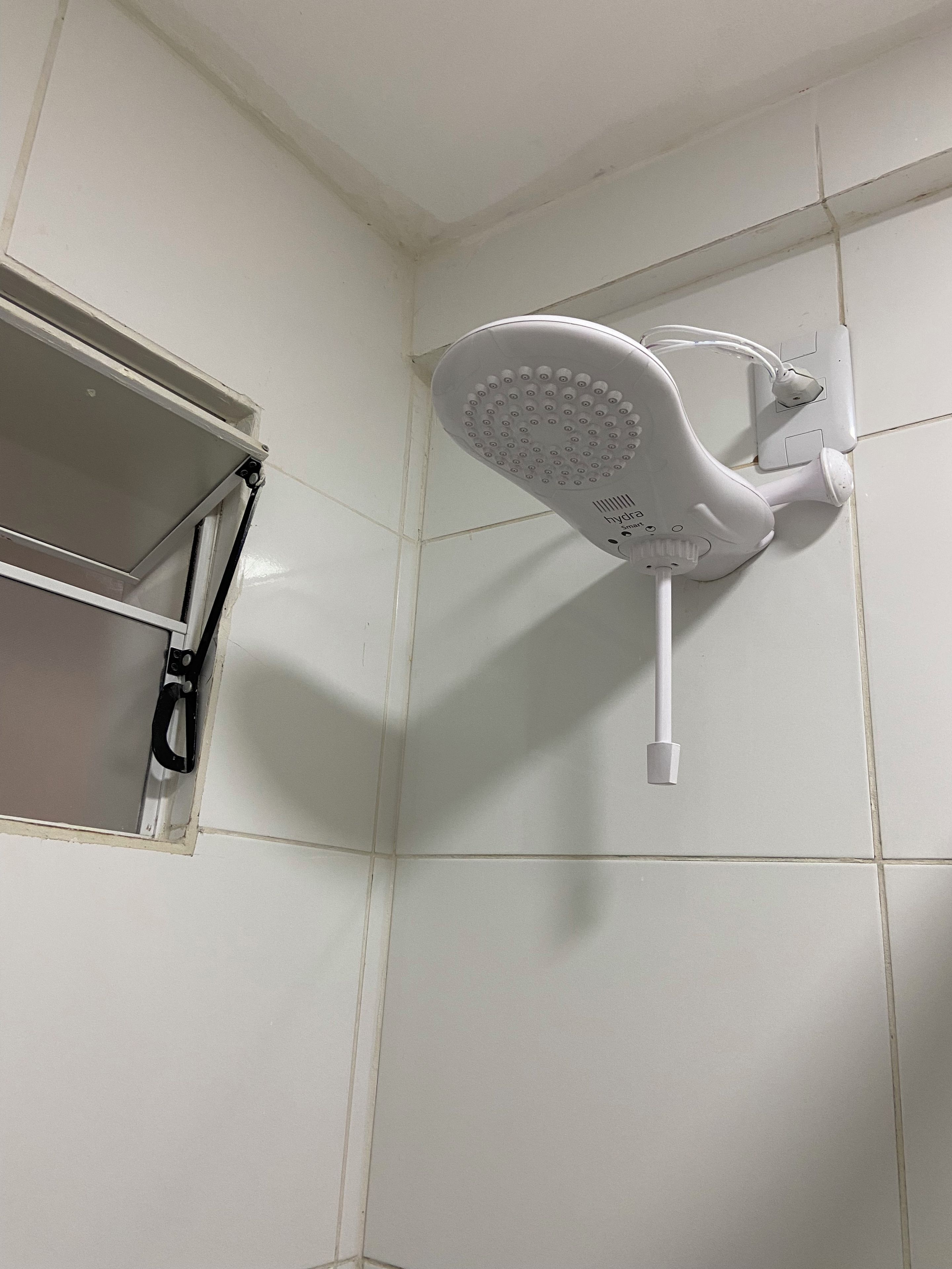 A showerhead mounted on a tiled wall with a shelf above it.