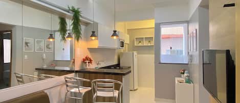 A modern kitchen with a central island, bar stools, pendant lighting, and a refrigerator.