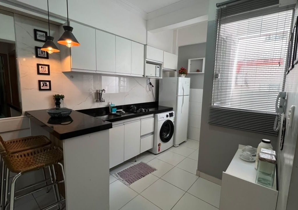 A modern kitchen with white cabinets, a black countertop, a washing machine, and a refrigerator.