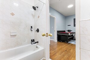 Ein Badezimmer mit Badewanne und Dusche, im angrenzenden Raum befindet sich ein Billardtisch.