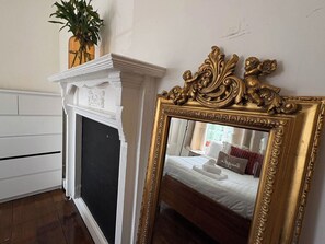 Ein Zimmer mit einem weißen Kamin, einem Spiegel mit goldener Rahmung und einem Bett mit weißer Bettwäsche.