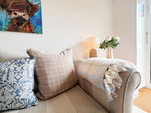 Sala de estar com sofá bege, almofadas estampadas, pintura de uma vaca, luminária e um vaso com flores.