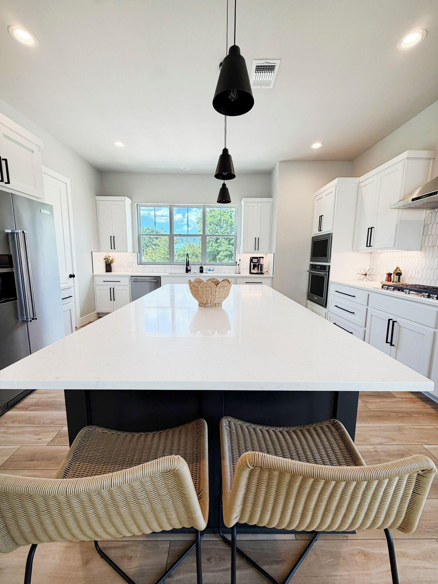 Een moderne keuken met een groot eiland, witte kastjes en een zwarte hanglamp.