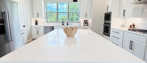 Una cucina moderna con una grande isola, mobili bianchi e una lampada a sospensione nera.