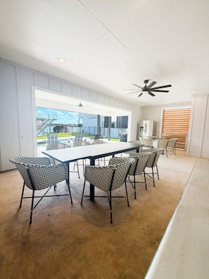 A modern dining area with a long table and patterned chairs, a ceiling fan, and a view of a swimming pool and outdoor area.