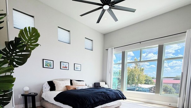Un dormitorio moderno con una cama grande, un ventilador de techo y vistas al exterior a través de amplios ventanales.
