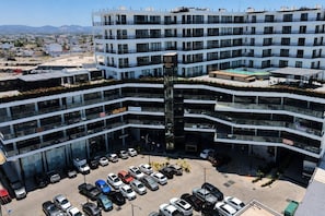 A multi-story hotel with a central atrium, a parking lot, and a view of the surrounding cityscape. - Dpto. nuevo a unos pasos de malecón y zona dorada (Mazatlán)