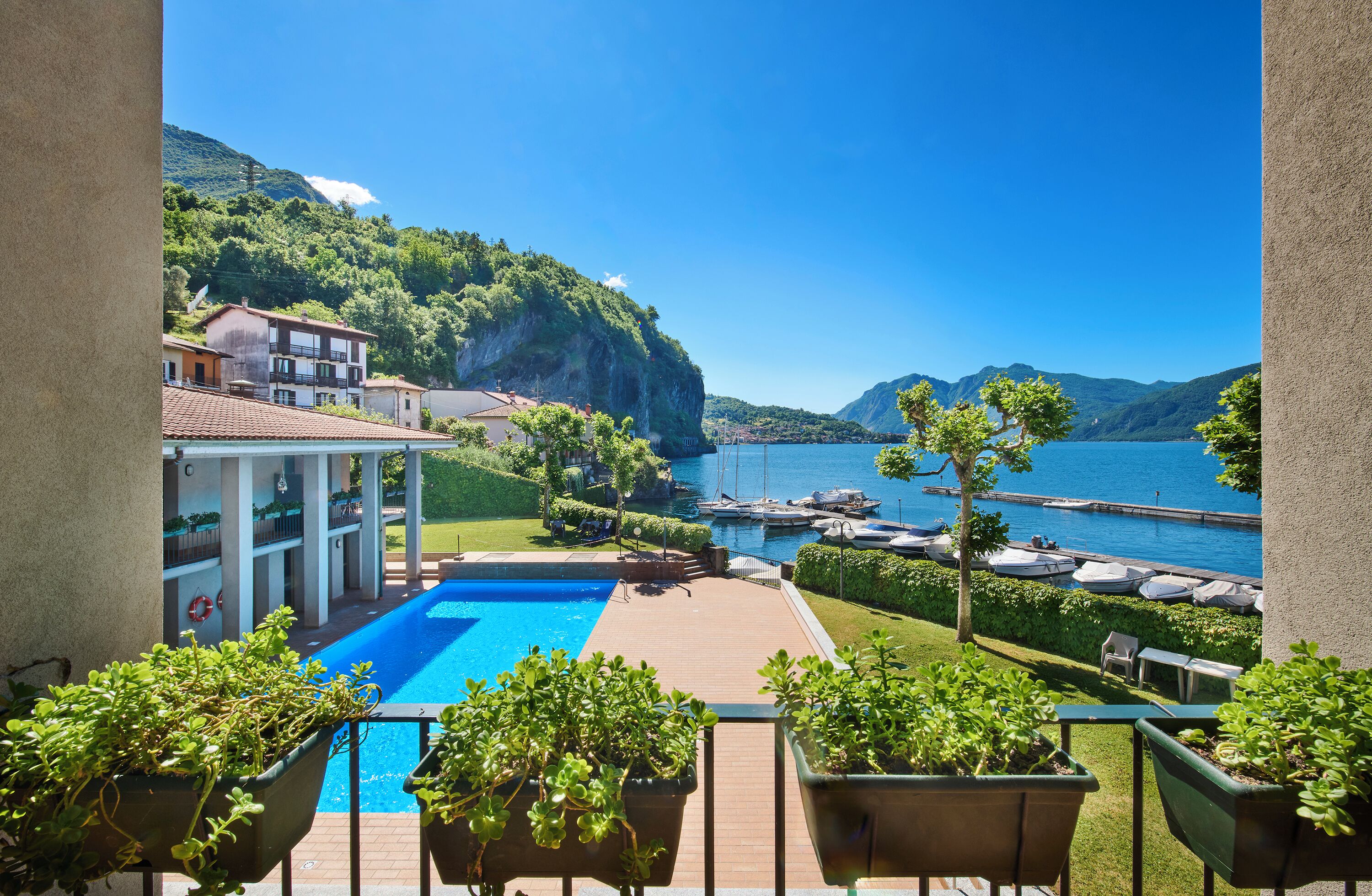 A poolside view with a clear view of a lake and boats, surrounded by greenery and buildings.