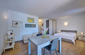 A modern bedroom with a bed, bedside tables, a desk, and a chair. There are wall-mounted lights, a framed picture, and a vase with flowers on the desk. - Domus Lario's Lake – stunning view, beach, swimming pool, and private parking (Lierna)