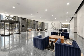 Eine moderne Lobby mit Glastür, Sitzgelegenheiten und einer Marmorwand mit geometrischem Muster.