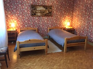 A room with two wooden beds, a wooden nightstand with a lamp, a chair, and a wall-mounted painting.