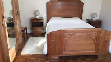 A wooden bed with a white mattress, a wooden nightstand with a lamp, and a small wooden cabinet.