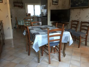Ein Essbereich mit einem Tisch für vier Personen, Holzkästen, einem Fernseher und einer Küche im Hintergrund.