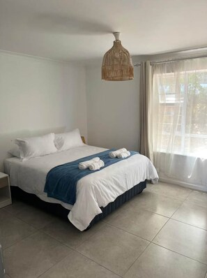 A bedroom with a bed, a nightstand, a blue throw blanket, and a hanging light fixture. - 2 Bedroom Pinelands Medical Leisure Apartment (Cape Town)