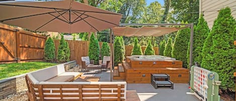Un patio trasero con terraza de madera, mobiliario exterior, un jacuzzi y un porche cubierto.