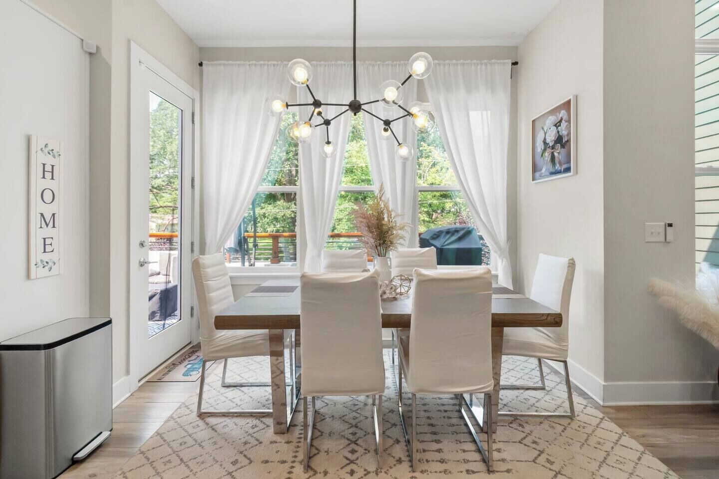 A dining area with a table, chairs, a chandelier, and a view of the outdoors.