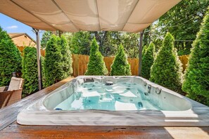 Ett bubbelbad i en trädgård med ett trästaket och vintergröna träd.