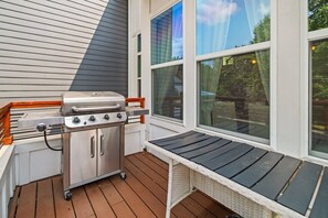 Eine Terrasse mit einem Edelstahlgrill, einem Holzboden und einem Fenster mit Blick auf einen Garten.