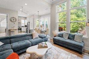 Ein modernes Wohnzimmer mit einem Ecksofa, einem Couchtisch und einem Essbereich mit einer Pendelleuchte.