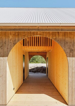 Une structure en bois dotée d’un toit incurvé et d’une passerelle centrale menant à un espace ouvert.