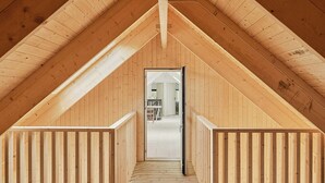 A wooden attic room with a sloped ceiling, a central doorway leading to an adjacent room, and a wooden railing along the walls. - Modern house in Staveström, Stockholm Archipelago (Ljusterö)
