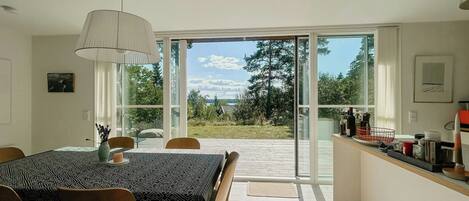 Comedor con mesa y sillas, una lámpara colgante y vista a un jardín mediante puertas de vidrio.