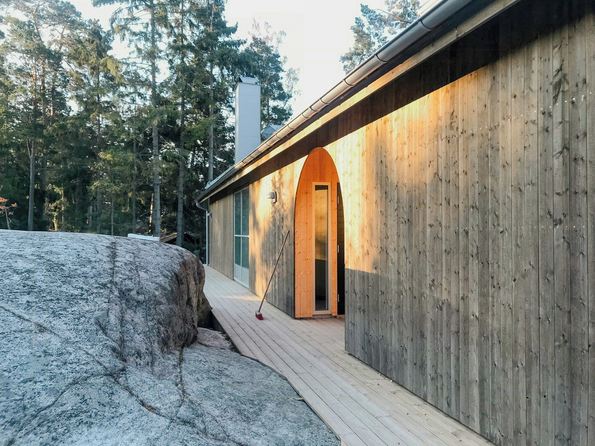 Ein hölzernes Gebäude mit einem großen Felsen im Vordergrund, einer Holzterrasse und freiem Blick auf den umliegenden Wald.