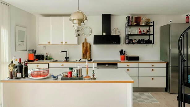A modern kitchen with white cabinetry, a central island, a black range hood, and a stainless steel refrigerator. - Modern house in Staveström, Stockholm Archipelago (Ljusterö)