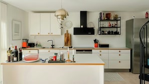Een moderne keuken met witte kasten, een centraal eiland, een zwarte afzuigkap en een roestvrijstalen koelkast.