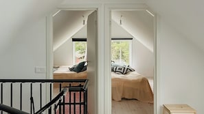 Een slaapkamer met schuine wand, een bed met een kussen met patroon, en een raam met uitzicht op groen.