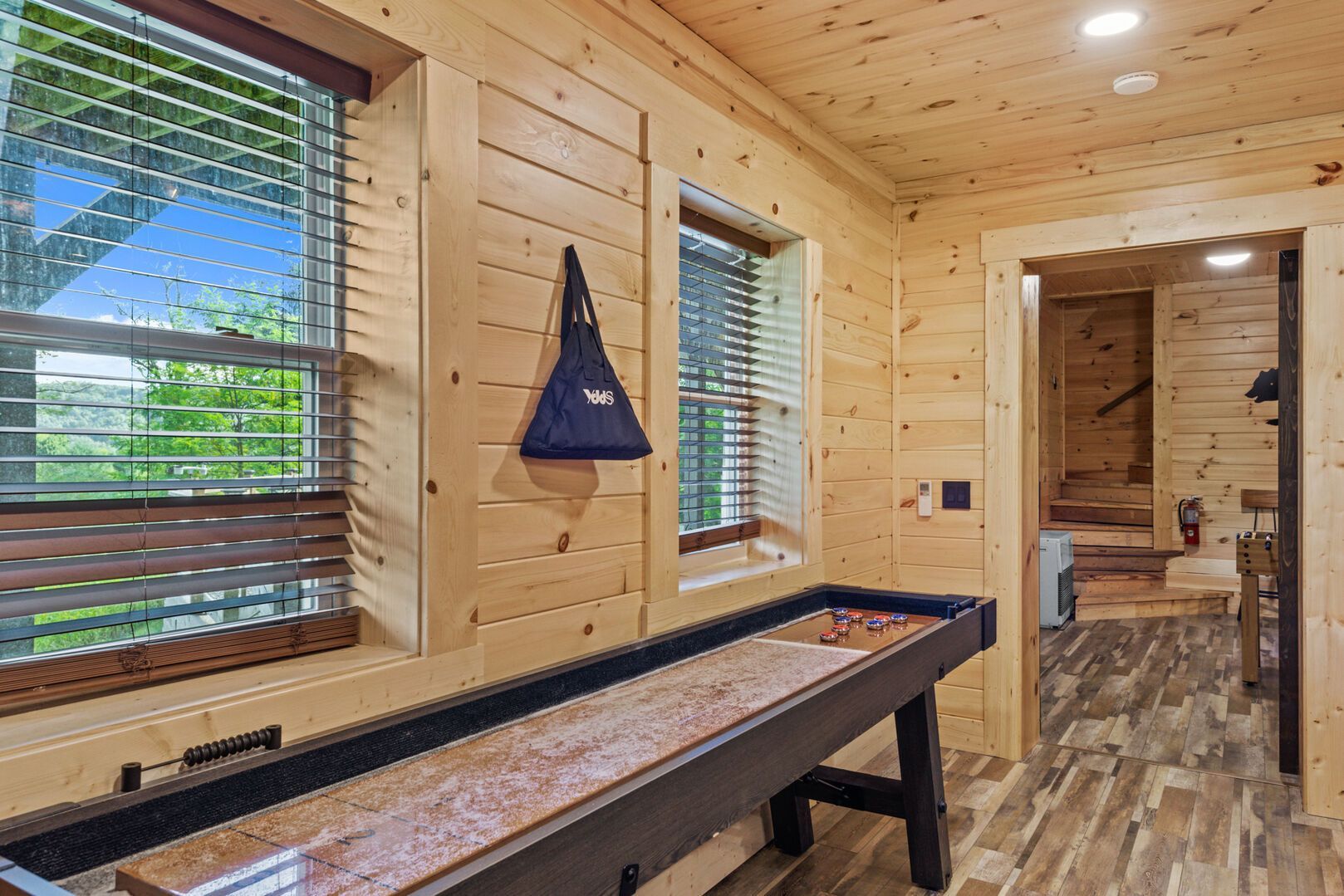 A wooden interior with a pool table, windows with blinds, and a hallway leading to another room.